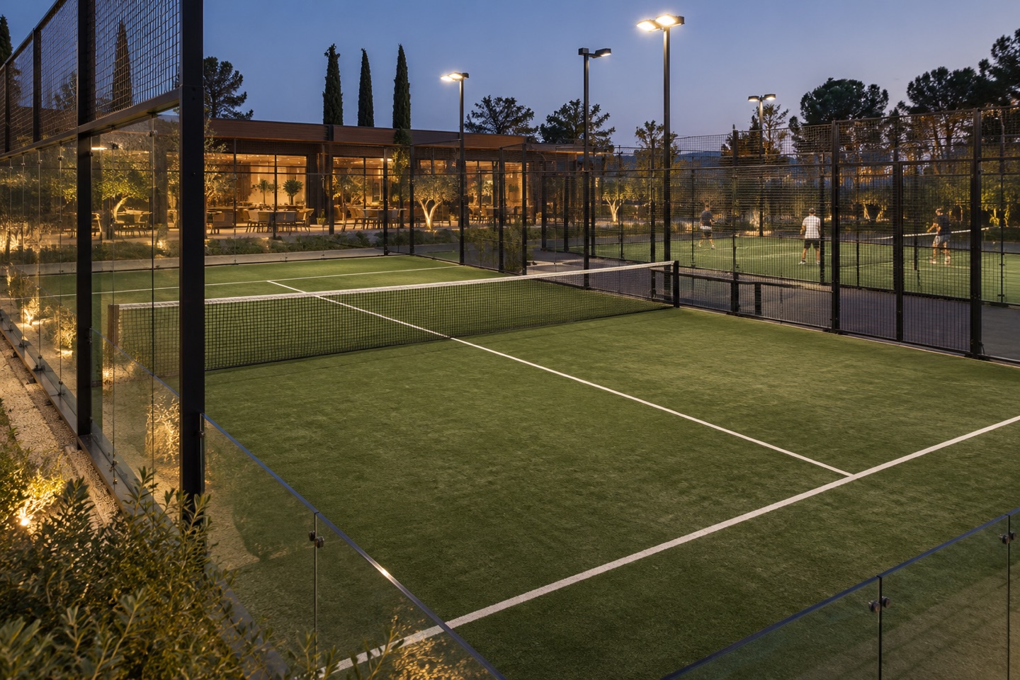 Floodlit padel courts with a clubhouse in the background.